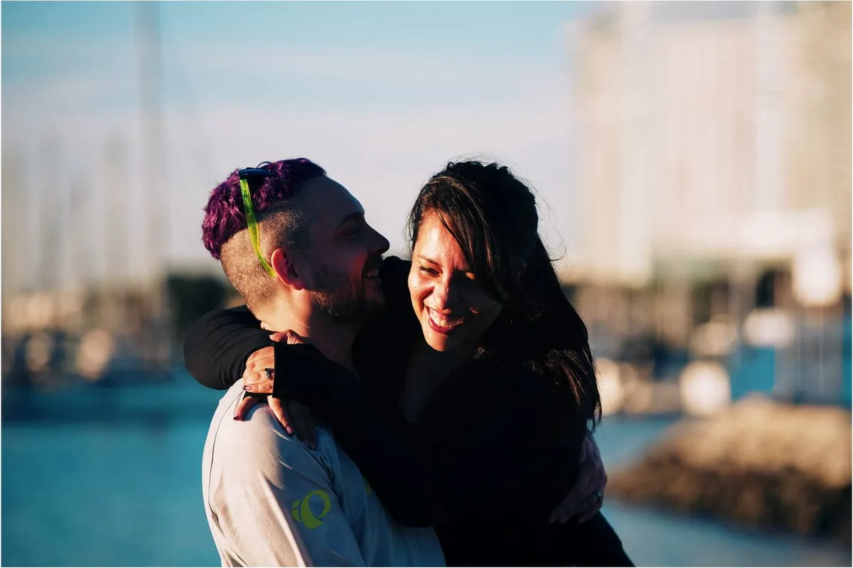 Saray with her arms around Jeremy, both of them laughing, the harbor behind them.